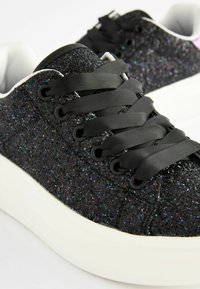 Schwarze Glitzersneaker mit strukturiertem Obermaterial, schwarzen Satin-Schnürsenkeln und einer weißen Gummisohle. Abgerundete Zehenform und Low-Top-Design.