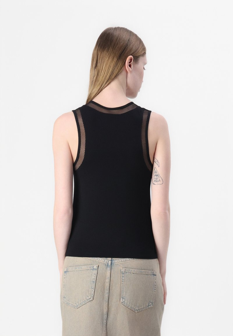 Top negro sin mangas con detalles de malla alrededor de los hombros, textura suave, diseño ajustado y cuello alto. Tatuaje visible en el brazo.