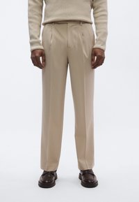 Beige skreddersydde bukser med rett passform, laget av mykt stoff, med folder og jevn tekstur, brukt sammen med mørkebrune sko.