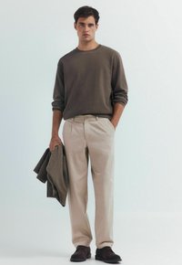 Housut khaki-beige rentoa fitiä, yhdistettynä teksturoituun ruskeaan pitkään hihaan. Tummanruskeat kengät, pidellen yhteensopivaa villapaitaa.