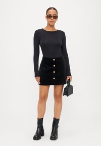 Melnas garām piedurknēm blūze, melna korduroja svārku ar zelta pogām, melnas augstpapēžu zābaki, lielas saulesbrilles un maza melna rokassoma.