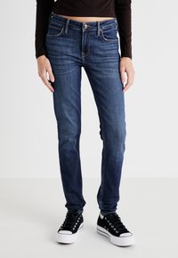 Tmavomodré džínsy so Slim fit strihom, ktoré majú päť vreciek, medený steh a zips. V kombinácii s čiernymi teniskami.