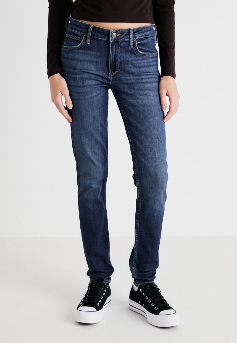 Tmavomodré džínsy so Slim fit strihom, ktoré majú päť vreciek, medený steh a zips. V kombinácii s čiernymi teniskami.