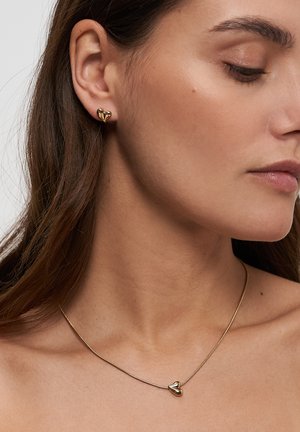 Goldkette mit herzförmigem Anhänger und passenden Ohrsteckern in Herzform. Schlankes Design, glatte Textur, minimalistisches Äußeres.