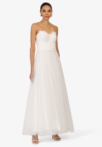 Robe blanche sans bretelles avec un corsage en dentelle florale et une jupe en tulle fluide. Présente un décolleté en cœur et des détails délicats.