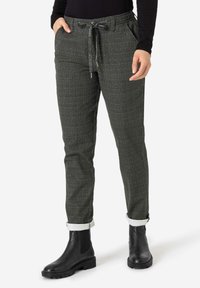 Dark green plaid trousers with an elastic waistband, drawstring detail, and rolled cuffs, paired with black ankle boots.