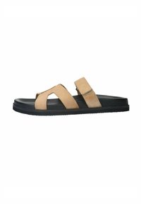 Beige suède sandalen met een zwarte rubberen zool hebben kruis- en verstelbare enkelbandjes, en bieden een casual open teen ontwerp.
