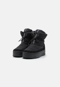 Botas negras aisladas con parte superior acolchada, cierre de cordón, detalles de ante y suela gruesa con textura. Presenta detalles de marca en la lengüeta.