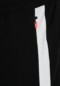 Zwarte sportieve shorts met een witte zijstreep, een kleine zwarte ritszak met een rode trekband en een elastische tailleband.