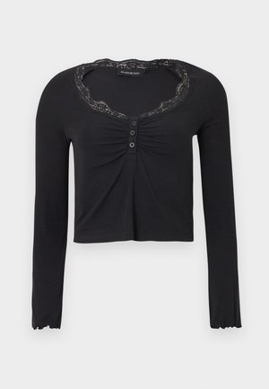 Musta pitkähihainen paita, jossa pitsireunuksella varustettu pääntie, kerrostettu edusta ja kolmen napin kiinnitys, hieman lyhennetty malli.