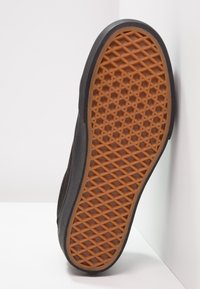 Semelle de chaussure avec une semelle extérieure en caoutchouc marron présentant un motif de crampons en losange et hexagonal, sur un fond blanc d'angle.