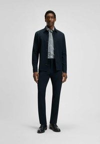Giacca navy con bottoni, camicia a quadri, pantaloni scuri e scarpe nere. Design slim fit con un aspetto strutturato e dettagli minimi.