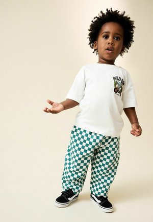 White cotton t-shirt with "WILD" graphic, paired with green and white checkered pants. Black sneakers with white sole. Casual outfit.