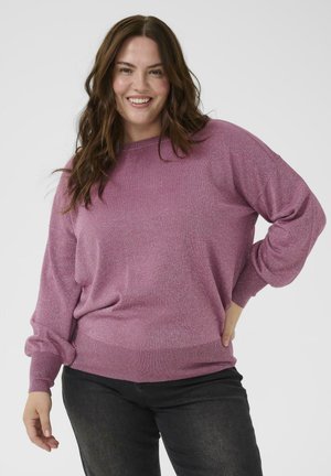 Rosa, glitzernder Pullover mit runder Ausschnitt, lockerer Passform und langen, leicht puffigen Ärmeln. Gerippter Saum und Bündchen. Kombiniert mit dunkelblauen Jeans.