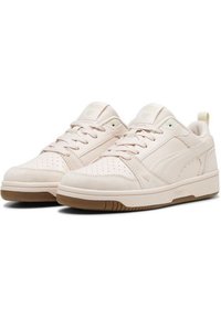 Paire de baskets basses beige clair avec lacets, zone des orteils perforée et semelles couleur gomme, légèrement inclinée vers la droite.