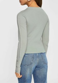 Light green ribbed sweater with long sleeves, featuring button accents on the cuffs, paired with blue denim high-waisted jeans.