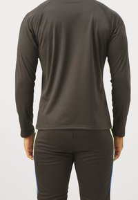 Långärmad träningsoverdel i mörkgrått, tillverkad av ett mjukt och lätt tyg. Har en rundad halsringning och raglanärmar. Kombineras med åtsittande svarta byxor.