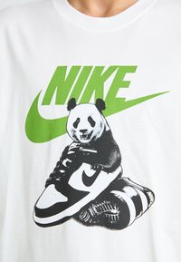 Hvid bomulds T-shirt med et grønt Nike-logo, en illustration af en panda på sort og hvid sneakers med detaljerede teksturer.