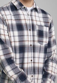 Grijze, marineblauwe en oranje geruite flanellen shirt, met knopen en een borstzak, bruine knopen, textuurstof, lange mouwen.