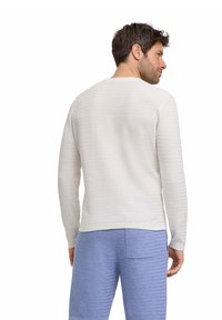 Weißes strukturiertes Langarmshirt mit Rundkragen, kombiniert mit blauen gemusterten Shorts, die über eine Gesäßtasche verfügen.