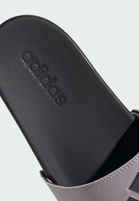 Adidas šľapka s čiernou textúrovanou podrážkou s vyrazeným logom a levanduľovým remienkom s detailným prešívaním a hladkým zakončením.