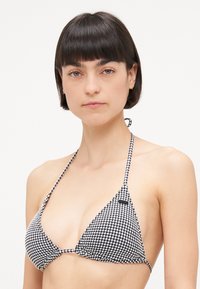 Svart og hvit rutete bikini-topp laget av stoff med trekantet design. Har tynne bånd og en liten merkevarelogo.