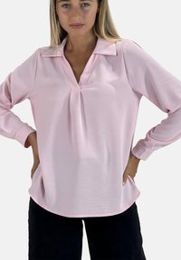 Lichtroze blouse met een V-hals en kraag, lange mouwen en een A-lijnvorm. Gemaakt van gladde stof met een subtiele textuur en zonder zichtbare patronen.