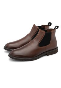 O pereche de cizme Chelsea din piele maro cu panouri elastice negre pe lateral și cârlige de prindere, pe un fundal alb.