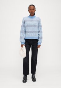 Pull tricoté bleu clair avec un motif texturé, présentant un col montant et des poignets côtelés, associé à un jean noir à jambe droite et un sac blanc doux.