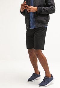 Shorts noirs, T-shirt bleu et veste bomber foncée associés à des baskets navy. Tissu lisse, shorts de longueur genou et style décontracté.