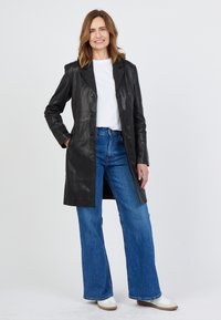 Schwarze Lederjacke mit maßgeschneidertem Design, einreihiger Knopfleiste und Reverskragen, kombiniert mit geraden blauen Jeans und weißen Sneakers.