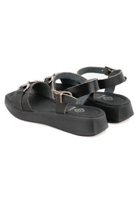 Schwarze Sandale mit mehreren verstellbaren Riemen, flacher Fußbett und dicker Sohle. Verfügt über metallische Akzente und ein strukturiertes Innenfutter.