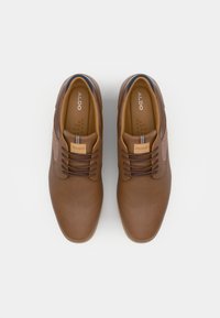 Chaussures en simili cuir marron à lacets, avec une texture lisse, dotées d'un accent bleu contrasté et d'une pièce en cuir beige. Design simple et arrondi.