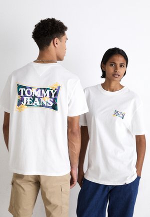 Camisetas de algodón blancas con el logo "TOMMY JEANS" en un diseño floral colorido en la parte posterior y un logo más pequeño en el bolsillo delantero.
