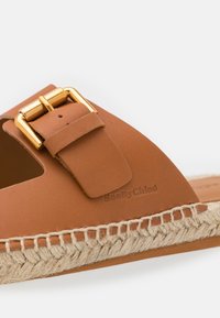 Sandale en cuir marron avec boucle dorée, coutures visibles, semelle en jute tressée et marquage embossé "SeeByChloe" sur le côté.