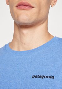 Tricou din bumbac albastru cu mâneci scurte, decolteu rotund și un logo "patagonia" negru pe partea stângă a pieptului. Textură netedă.