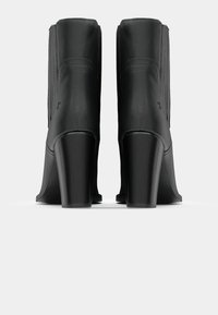 Botas de couro pretas até ao tornozelo com biqueira arredondada, saltos altos em bloco, detalhes de costura vertical e textura suave. Design minimalista.