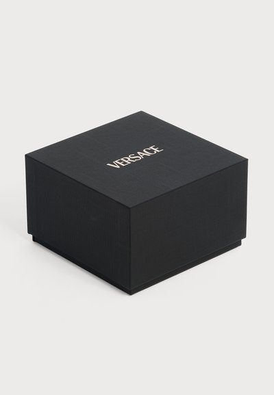 Boîte carrée noire avec surface texturée et "VERSACE" écrit en lettres majuscules au centre en haut.