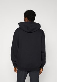 Hoodie preto com um grande capuz de duas camadas, mangas longas e punhos canelados. Feito de tecido suave com um ajuste descontraído.