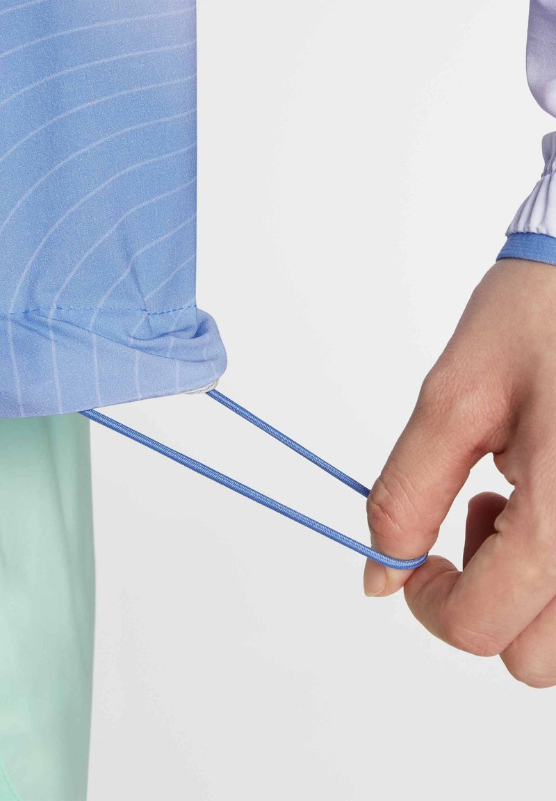 Lichtblauw sportshirt met horizontale strepen, voorzien van een elastisch koord aan de onderkant, hand dat het koord vasthoudt. Gladde textuur.