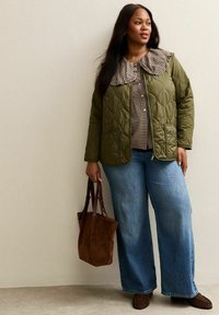 Quiltad grön jacka med en stor rutmönstrad krage, tillsammans med en rutmönstrad blus och vida blå jeans. Brun mocka tote-väska.