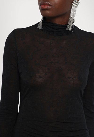 Tricou negru cu mânecă lungă și decolteu înalt, realizat dintr-un material transparent cu o textură florală subtilă. Accesorizat cu cercei statement.