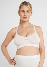 Lichtroze zwangerschapsbeha van zacht materiaal, met verstelbare banden en een centraal strikdetail. Glad, naadloos ontwerp voor comfort.