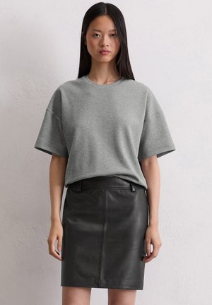 Gray oversized t-shirt with short sleeves paired with a fitted black leather skirt. Smooth fabric and clean lines characterize the outfit.