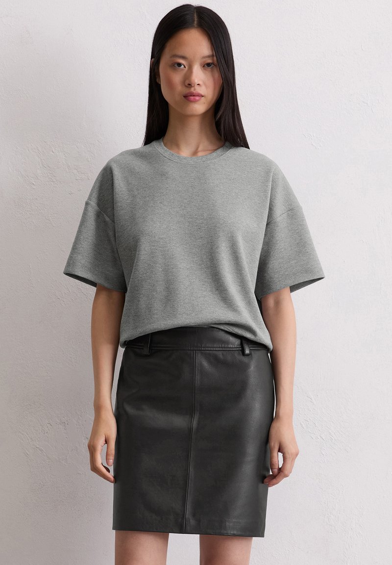 Gray oversized t-shirt with short sleeves paired with a fitted black leather skirt. Smooth fabric and clean lines characterize the outfit.