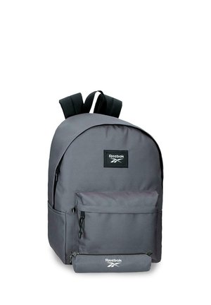 Mochila Reebok de color gris oscuro con bolsillo delantero con cremallera y correas negras para los hombros sobre fondo blanco.