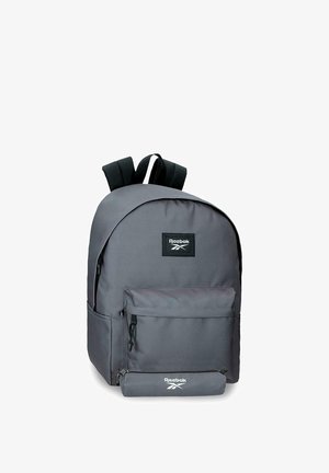 Mochila Reebok de color gris oscuro con bolsillo delantero con cremallera y correas negras para los hombros sobre fondo blanco.