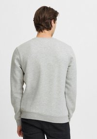 Sudadera gris hecha de una tela suave, con escote de crew y puños y dobladillo acanalados. El diseño es sencillo, sin gráficos visibles.