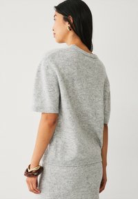 Lys grå kortærmet sweater i blødt strikmateriale. Har en rund hals, ribbede manchetter og en afslappet pasform. Enkel og minimalisk design.