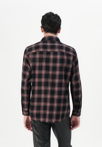 Camicia a quadri con colori nero, rosso e bianco. Maniche lunghe con colletto e bottone sul retro. Realizzata in tessuto morbido.